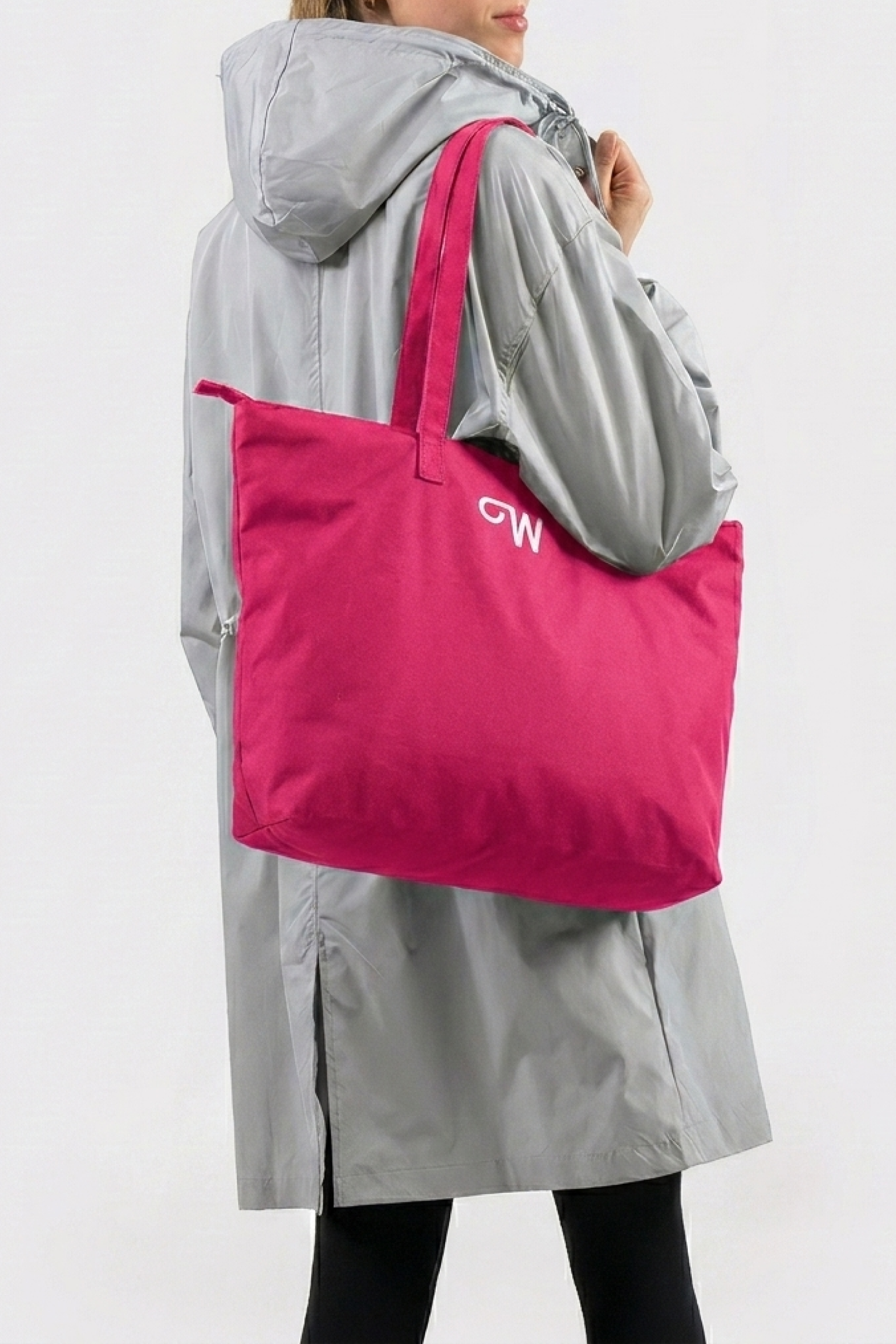 A person in a light gray hooded coat and black pants carries the Urban Slate Waterproof Bag, a large, bright pink travel duffel with a small white logo on the side, against a plain white background.