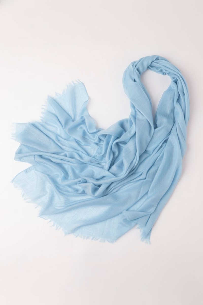 The looselyboho Sky Mist 100% Cashmere Scarf, in light blue with frayed edges, is displayed on a plain light surface and loosely gathered at one end.