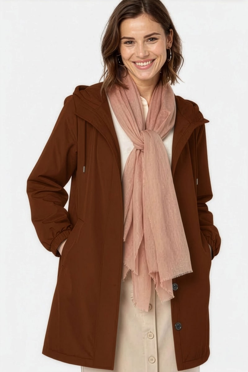 A woman smiles with her hands in her brown hooded coat pockets, wearing a looselyboho Sandstone Dune 100% Cashmere Scarf and a light button-front dress perfect for layering in winter.