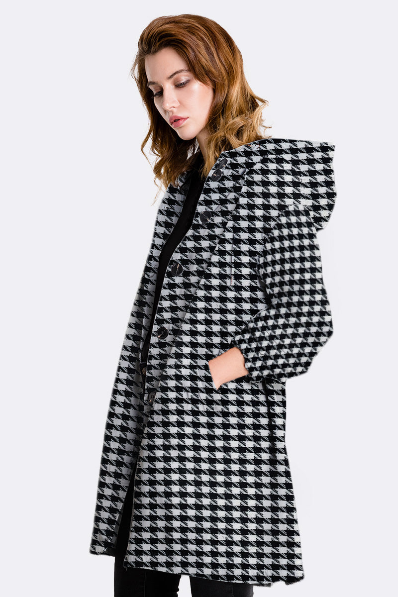 A woman with shoulder-length light brown hair wears the looselyboho HOUNDSTOOTH WINDBREAKER, featuring a black and white pattern and hood. She faces sideways against a plain light background, looking down.