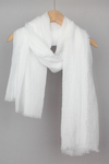 A white all-weather scarf hangs on a wooden hanger against a plain gray background. The Color-POP Scarf appears soft and slightly textured, with frayed edges giving it a casual, cozy look—a perfect pairing for looselyboho.