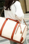 A person with long hair is carrying The Smart No-Wrinkle Foldable Travel Bag by The Windbreaker Jacket, which is large and white with brown straps and accents. The person is wearing a white top, and the background includes steps and a building with large columns.