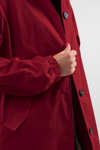 A person adjusts the lapel of a looselyboho Burgundy Blossom Windbreaker, showcasing its large buttons. The windbreaker features long sleeves with elastic cuffs, pockets, and a floral-patterned lining. Only the coat and the hand are visible.