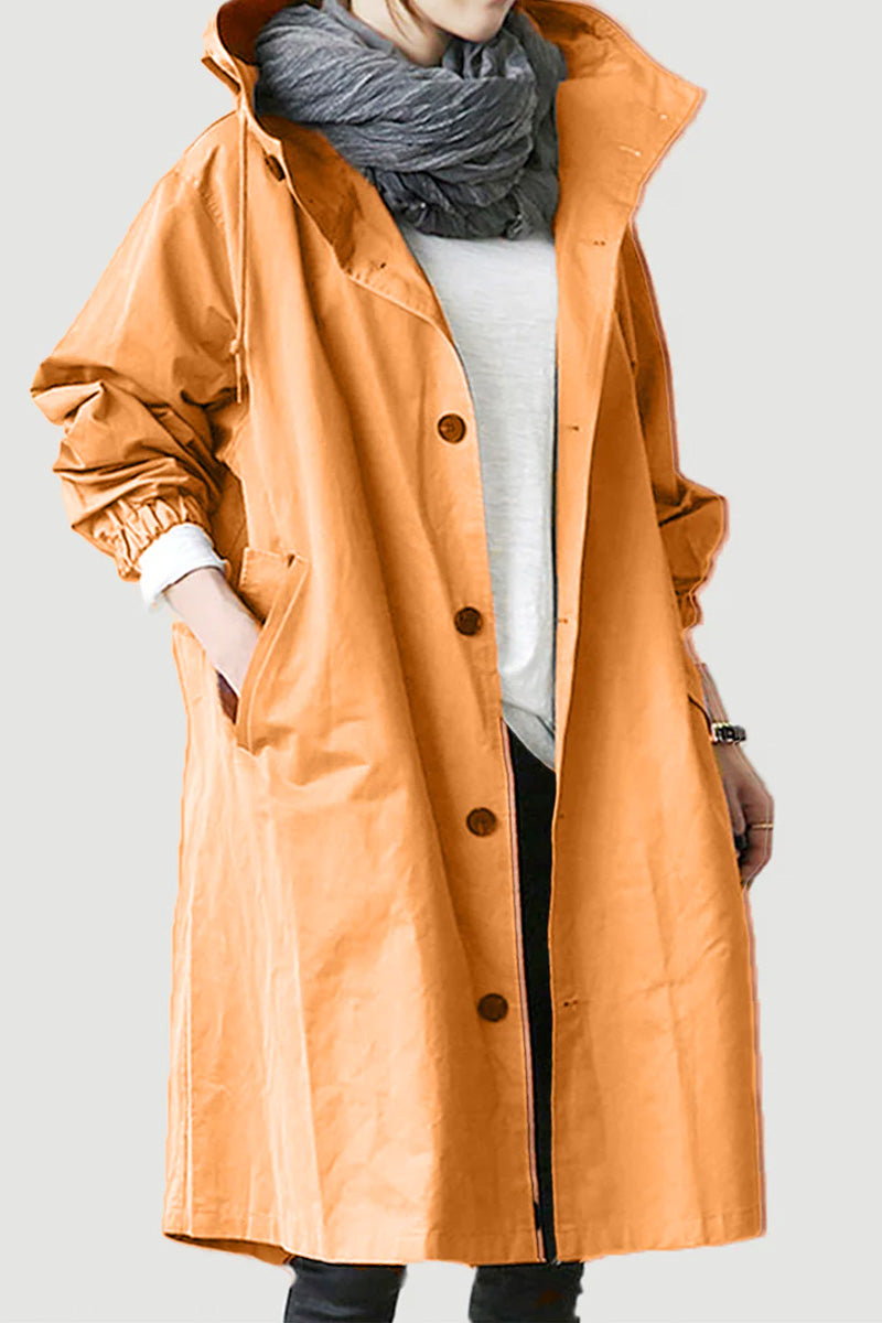 A person is wearing a timeless orange Water Resistant Oversized Hooded Windbreaker Rain Jacket by The WJacket, complete with black buttons. Their hands are tucked into the pockets of this versatile coat, and they are accessorized with a grey scarf and a white shirt underneath. Their face is not visible.