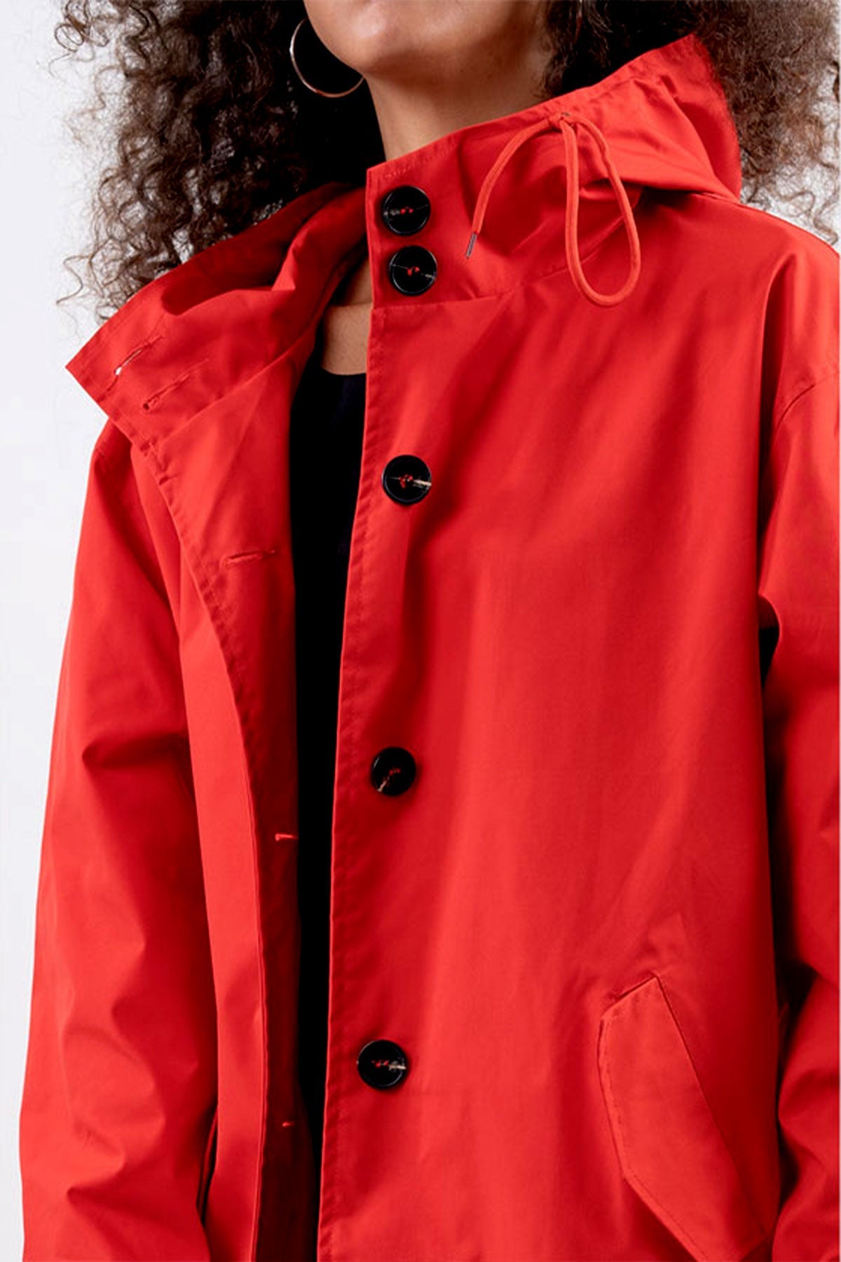 A person wearing The WJacket's Water Resistant Oversized Hooded Windbreaker Rain Jacket in bright red, featuring large black buttons and side pockets, exudes timeless style. The jacket, showcasing the versatility of a windbreaker, is partially unbuttoned to reveal a dark-colored garment underneath. Only the lower face and upper torso of the individual are visible.