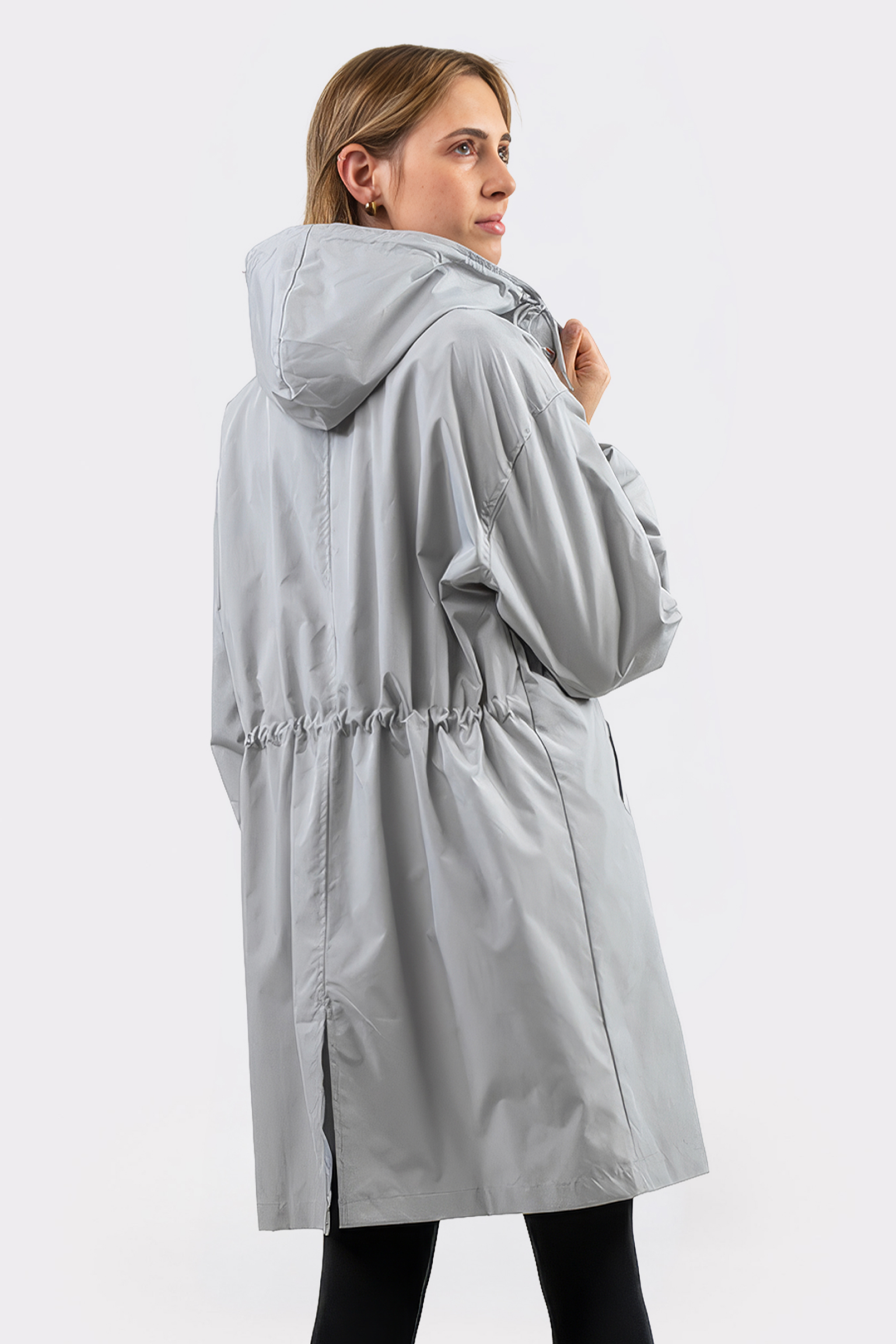 A person in the Icon Windbreaker Rain Jacket, light gray with a cinched waist and mid-thigh length, stands on a plain white background, facing away while looking over their shoulder.