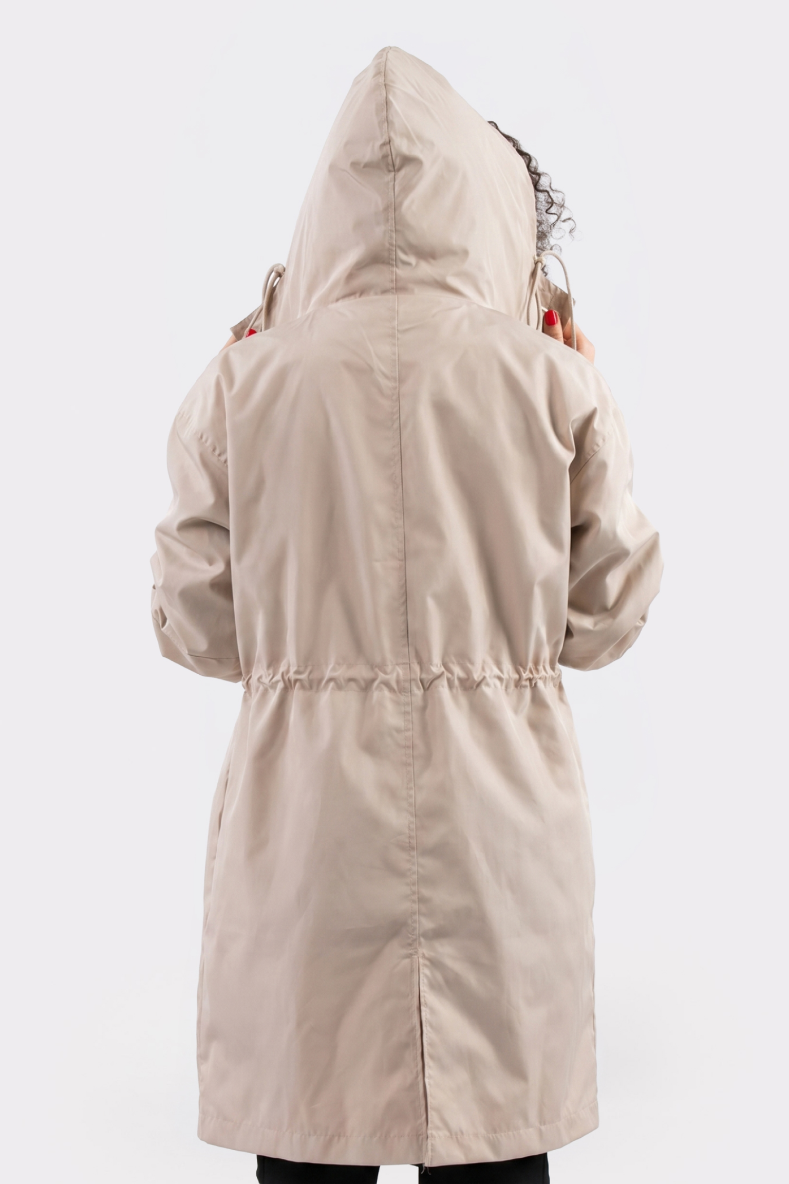 A person is shown from the back, holding the hood of The Water Resistant Hooded Oversized Windbreaker Rain Jacket in light beige. The background is plain white.