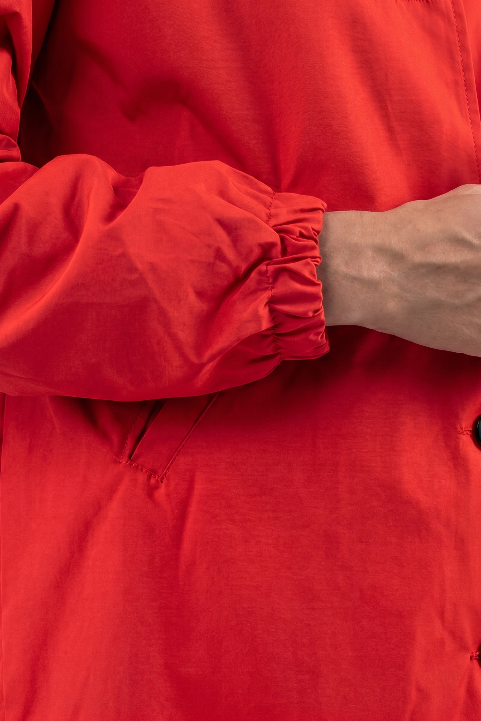 A close-up of a person wearing The Water Resistant Hooded Oversized Windbreaker Rain Jacket in red, featuring an elastic cuff, with part of their arm and hand visible against a plain background.