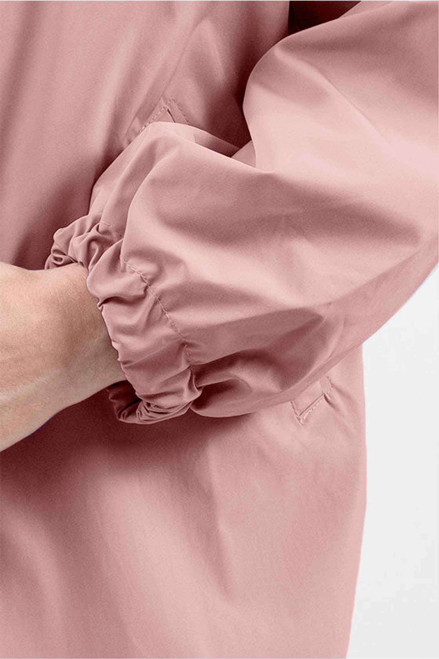 A close-up view shows a person’s arm wearing The Water Resistant Hooded Oversized Windbreaker Rain Jacket in pink, featuring an elastic cuff. The hand is partially visible against a plain, light-colored background.