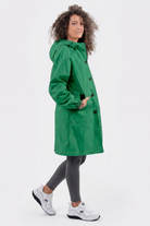 A person with curly hair is wearing the Icon Windbreaker Rain Jacket in green, paired with gray leggings and white sneakers. They stand against a plain white background, facing slightly to the side.