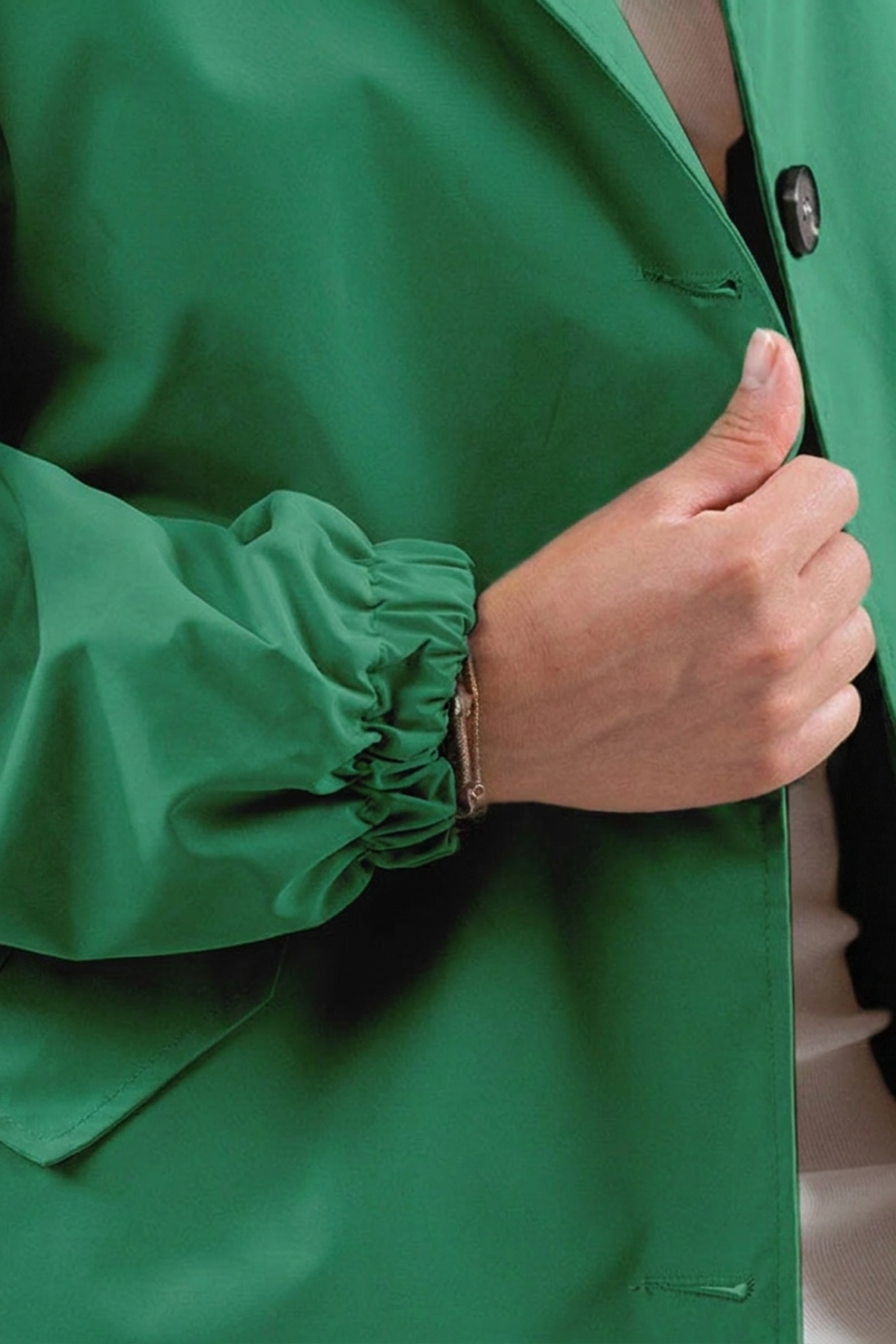 A hand holds closed The Water Resistant Hooded Oversized Windbreaker Rain Jacket, showing its green color and elastic cuffs; only the jacket and hand are visible.