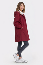 A woman stands in profile against a plain white background, wearing the Icon Windbreaker Rain Jacket with dark skinny jeans and white sneakers.