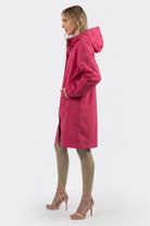 A woman stands in profile wearing the Icon Windbreaker Rain Jacket, beige fitted pants, and light pink high-heeled sandals against a plain white background.