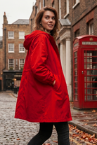 Wearing the Icon Windbreaker Rain Jacket, a person stands on a cobblestone street beside a classic red British phone booth, with brick buildings and autumn leaves in the background.