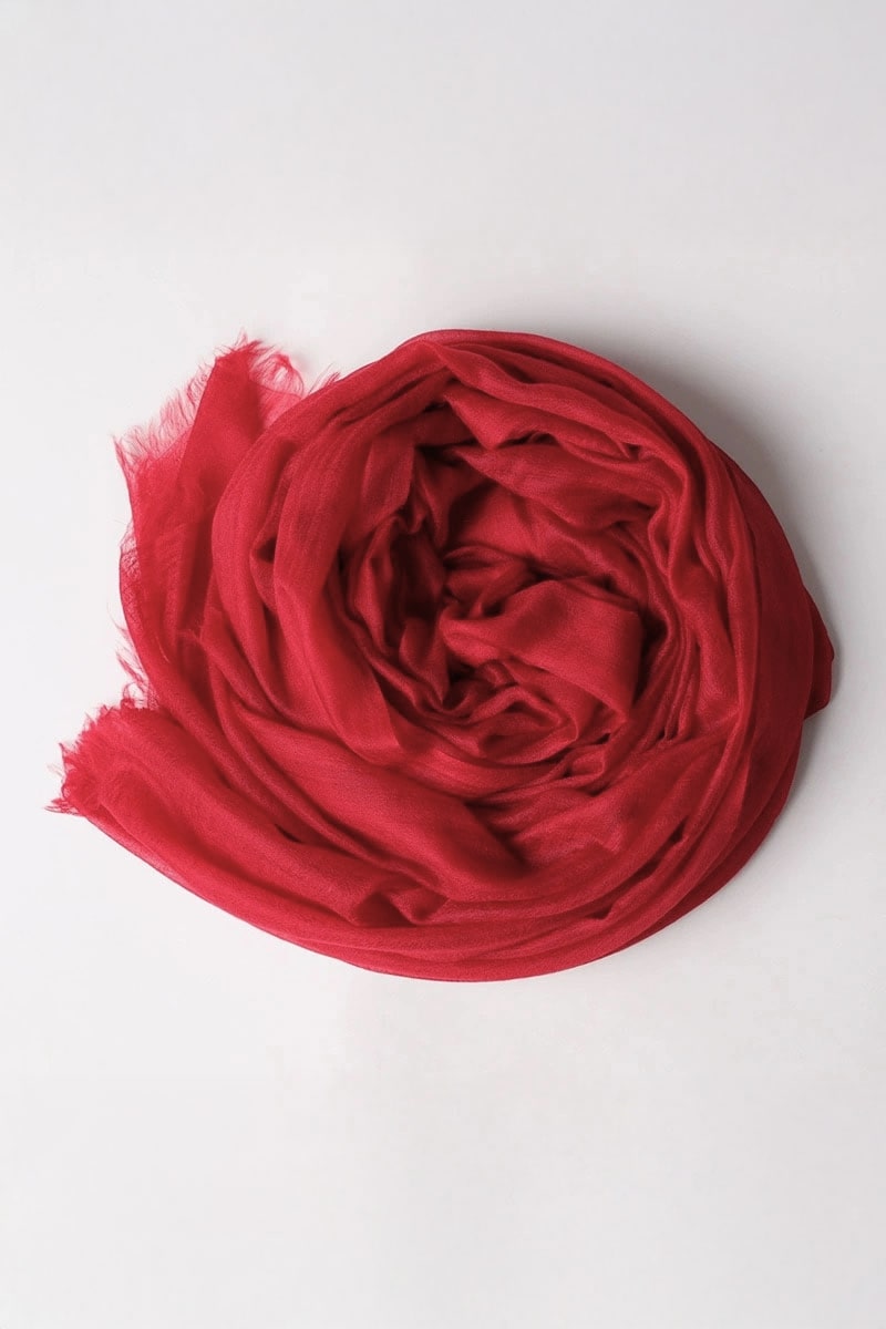 The Velvet Merlot 100% Cashmere Scarf by looselyboho, shown in a loose circle on a plain white background, features lightweight burgundy fabric with slightly frayed edges.