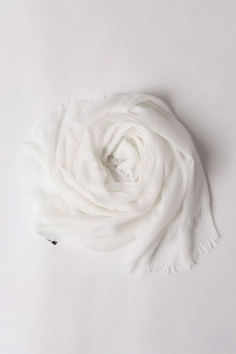The looselyboho Ivory Whisper 100% Cashmere Scarf, a lightweight ivory accessory with subtly frayed edges, is elegantly displayed in a circular shape on a plain white background.