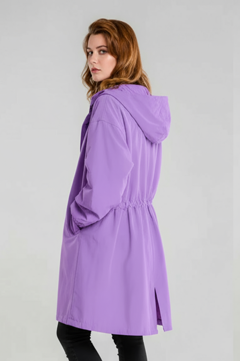A person with long, wavy light brown hair models the looselyboho SOFT LAVENDER WINDBREAKER with adjustable hood, gathered waist, and back slit, standing against a plain gray background.