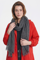 A person with light brown hair wears a bright red buttoned jacket and the Lightweight Linen Scarf in dark gray, featuring large texture and an ultra-breathable design, while standing against a plain white background facing the camera.