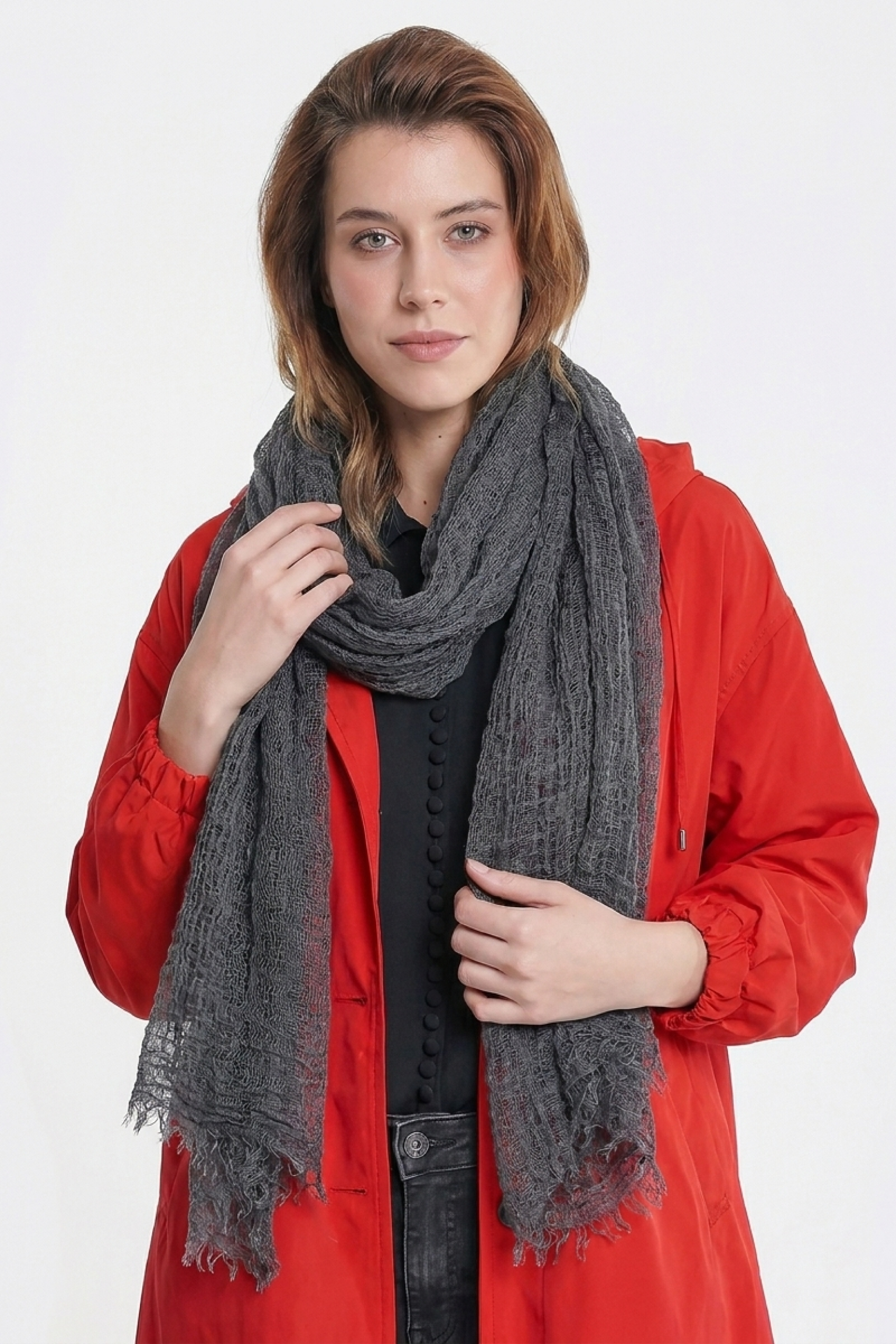 A person with light brown hair wears a bright red buttoned jacket and the Lightweight Linen Scarf in dark gray, featuring large texture and an ultra-breathable design, while standing against a plain white background facing the camera.
