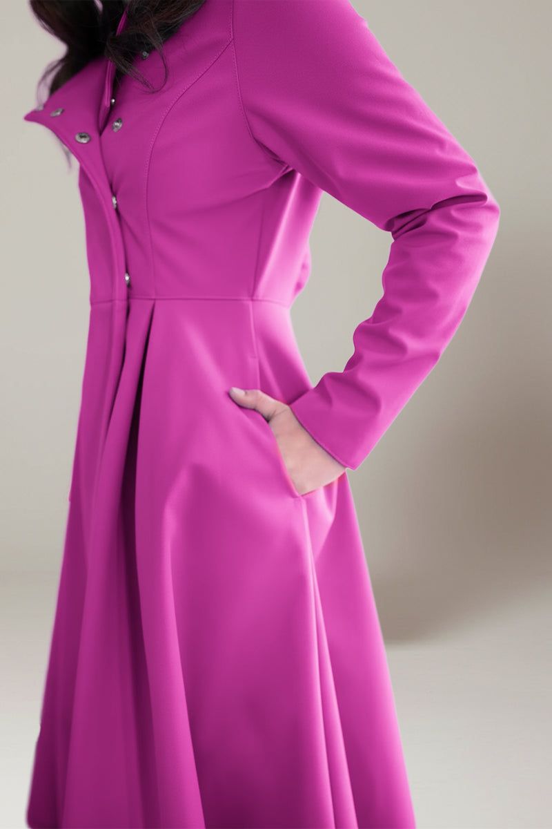 A person stands with one hand in their pocket, modeling the looselyboho Water-Repellent Rain & Shine A-Line Hooded Raincoat—a long-sleeved, magenta women’s raincoat with buttons and pleats. The head is out of frame.