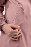 A close-up shot of a person's hand with neatly manicured nails placing or removing an item from the front pocket of a PASTEL PINK WINDBREAKER. The sleeve of The Windbreaker Jacket has elastic at the wrist, adding a touch of stylish clothing to the scene.